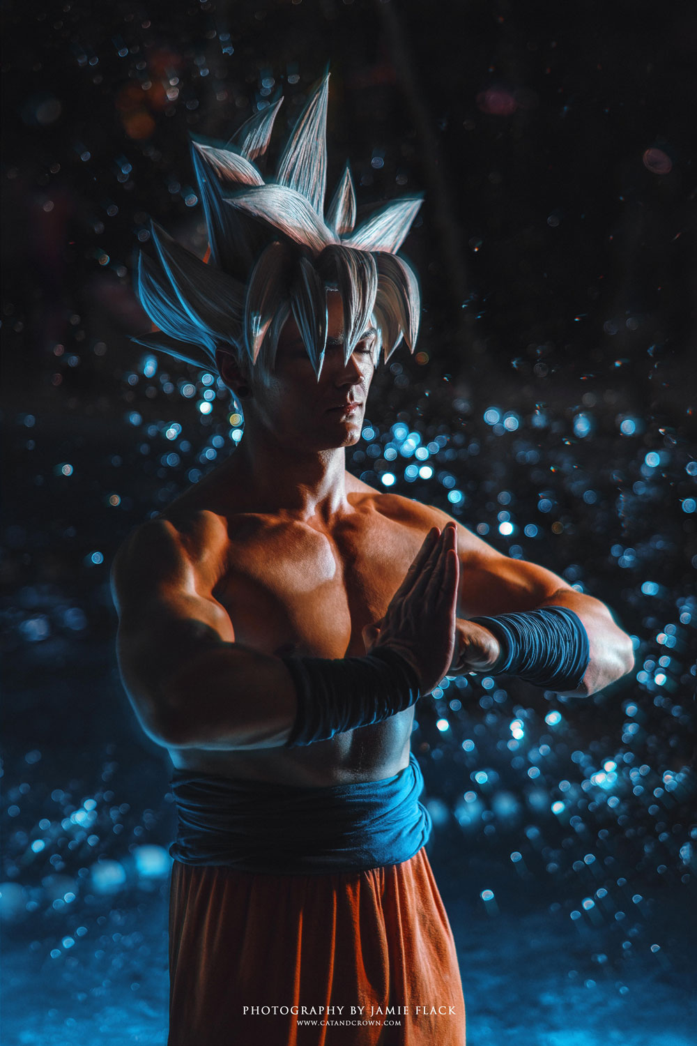 Der Cosplayer Minney verkleidet sich als Super-Saiyajin Goku aus Dragonball. Er hat blonde Haare und trägt einen orangenen Kampfanzug. In einer meditierenden Pose steht er vor einem schwarzen Hintergrund, der mit blauen Lichteffekten akzentuiert ist.