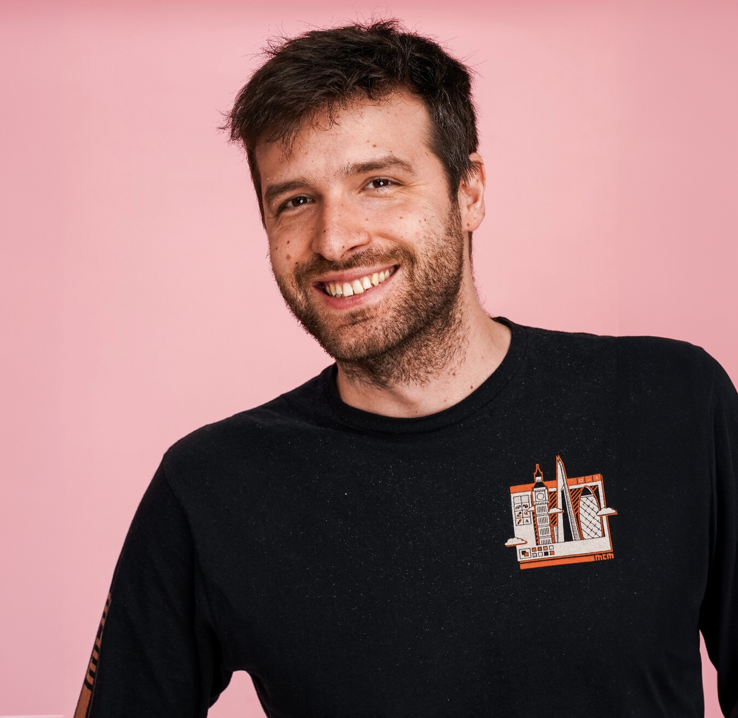 Der Synchronsprecher lächelt in die Kamera vor einem rosanen Hintergrund.