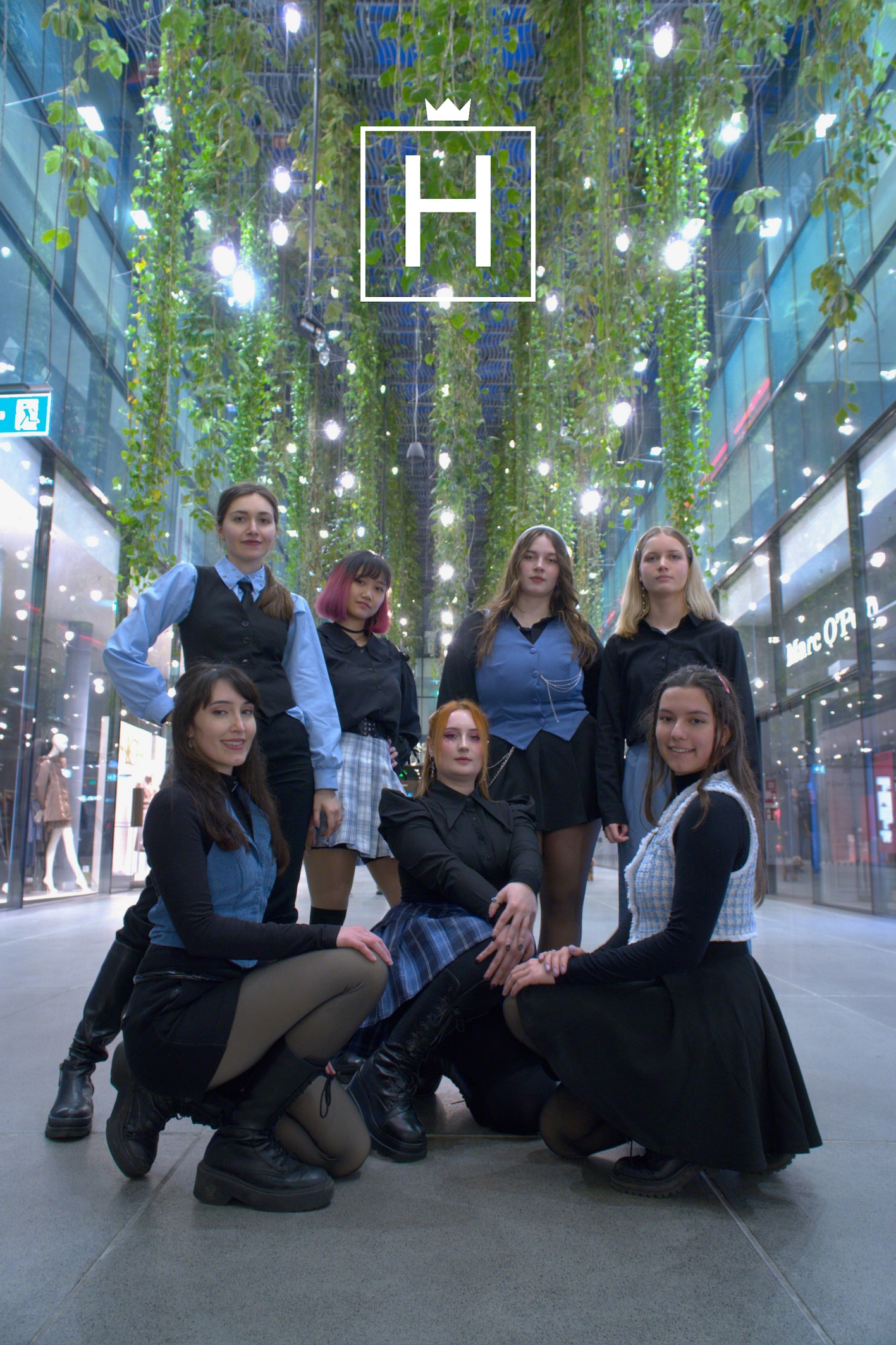 K-Pop Tanzgruppe Hal0queens, 7 Mitglieder posieren in die Kamera, das Logo der Gruppe oben mittig zu sehen