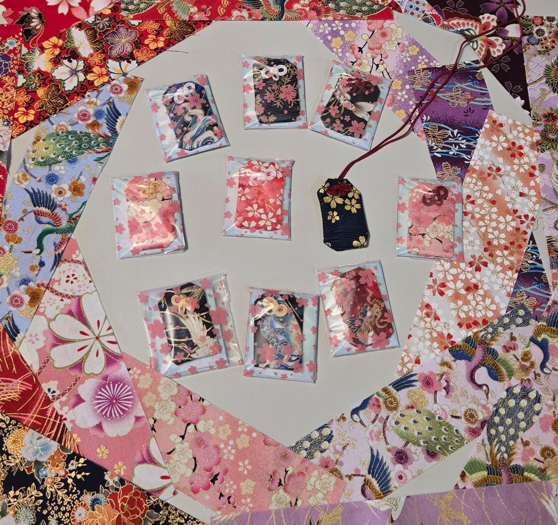 Ein paar vollendete Omamori umringt von Stoffproben mit unterschiedlichsten Mustern.